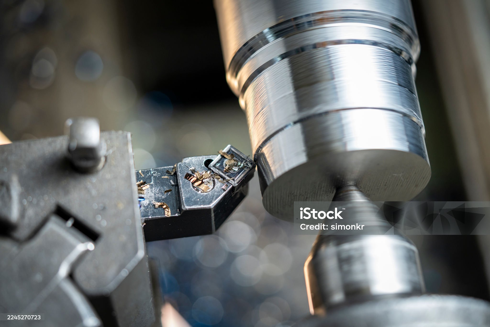 Close-up view of a precision metal lathe turning a cylindrical part. The lathe tool steadily shapes the metal, with fine metal shavings visible. The process takes place in an industrial workshop, showcasing the precision and skill involved in machining.